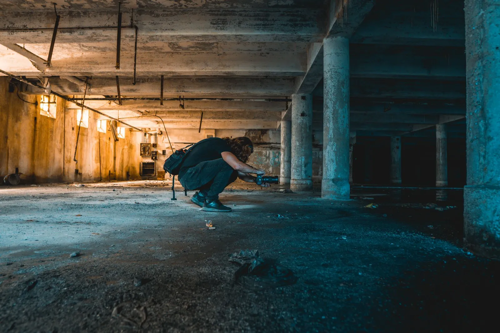 A photographer crouches in an abandoned, dimly lit industrial warehouse.